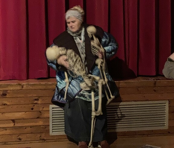 Eine Frau sitzt auf der Bühne vor einem roten Vorhang.