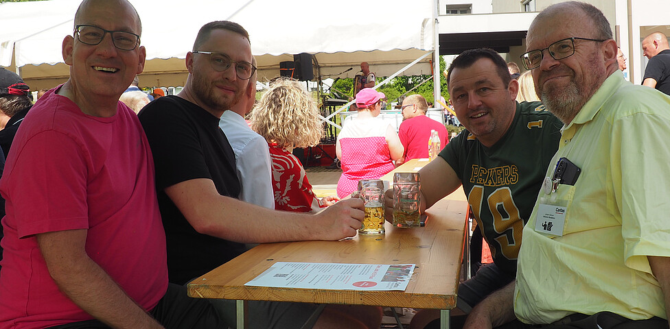 Vier Männer sitzen unter einem Sonnenschirm auf einem Biertisch