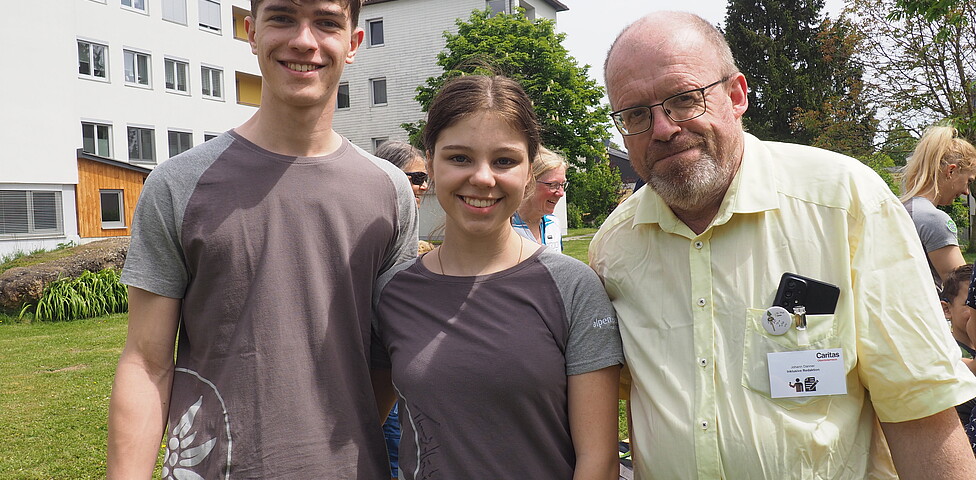 Zwei Jugendliche und ein Mann stehen vor einem Gebäude im Freien und lachen in die Kamera